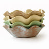 Stack of ceramic ruffled bowls in various colors on a white background
