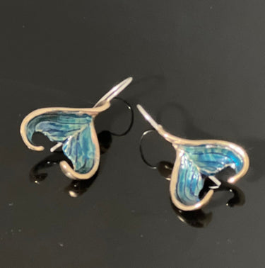 A pair of handmade Bronze earrings featuring curved, fin shapes with  blue patina, displayed on a dark reflective surface.