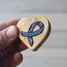 Wooden heart-shaped object with a blue ribbon symbol held by a hand against a neutral background