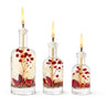 Three lit candles in glass bottles with floral elements against a white background