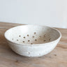 Speckled ceramic colander on a wooden surface with a white background