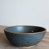 Dark blue ceramic bowl on a wooden surface with a light gray background