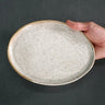 Hand holding a speckled ceramic plate against a dark background