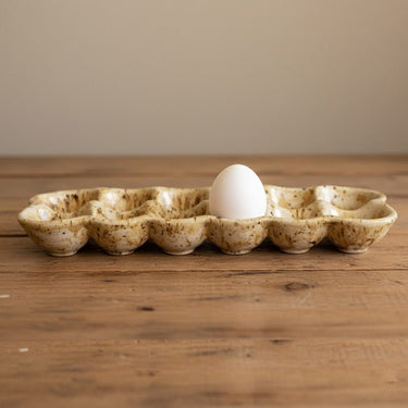 Ceramic egg tray with a single white egg on a wooden surface