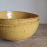 Two yellow ceramic bowls stacked on a wooden surface with a neutral background