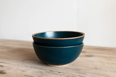Two dark blue ceramic bowls stacked on a wooden surface with a light gray background