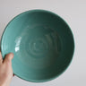 Teal ceramic bowl held by a hand against a plain background