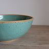 Turquoise ceramic bowl on a wooden surface with a plain background