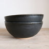 Two black ceramic bowls stacked on a wooden surface with a white background