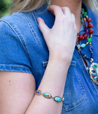 Person wearing a colorful beaded necklace and turquoise bracelet with a blue denim shirt.