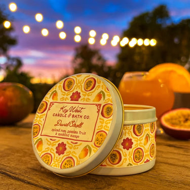 Candle tin with fruit design on a wooden surface with a sunset background