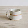 White ceramic mug with a gold band on a wooden surface