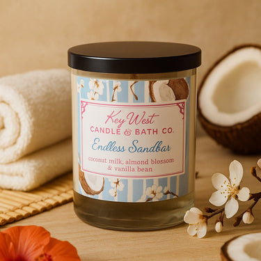 Candle with a label from Key West Candle & Bath Co. with towel and flowers in the background