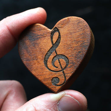 Wooden heart-shaped object with a music note symbol held by a hand against a dark background