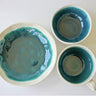 Two ceramic bowls with teal interior and beige exterior on a white background