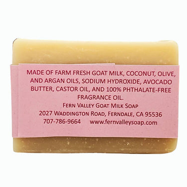 Bar of soap with a pink label detailing ingredients and contact information on a white background