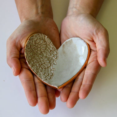 Heart-shaped ceramic piece held in hands against a plain background