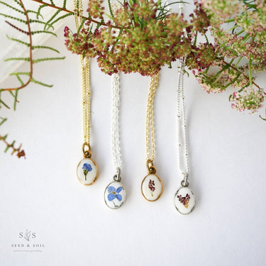 Four necklaces with floral pendants on a white background with greenery.