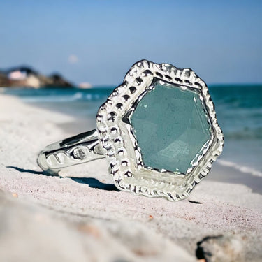 Silver ring with a light blue gemstone on a sandy beach