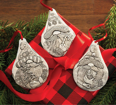 Three decorative Christmas ornaments with intricate designs on a red ribbon with plaid pattern, surrounded by greenery.