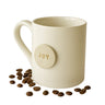 Beige mug with 'JOY' button and scattered coffee beans on a white background