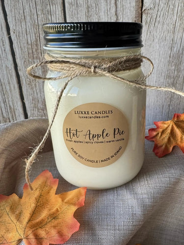 Candle in a mason jar labeled 'Hot Apple Pie' with autumn leaves on a wooden surface