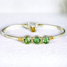Gold bracelet with green gemstones on a white background