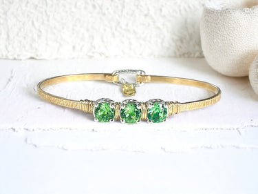 Gold bracelet with green gemstones on a textured white background