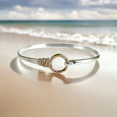 Silver bracelet with gold accents on a sandy beach with ocean in the background