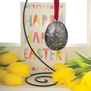 Decorative Easter egg ornament with a red ribbon, yellow tulips, and a colorful 'Happy Easter' sign.