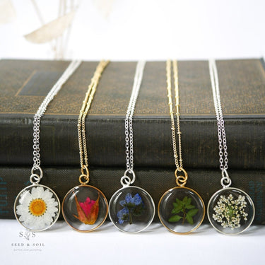 Five necklaces with floral Pressed Botanical Pendants on a stack of books.