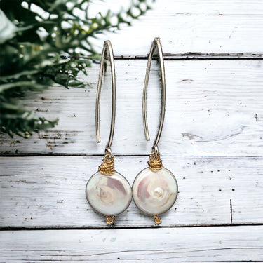 Pair of pearl earrings on a wooden surface with greenery in the background