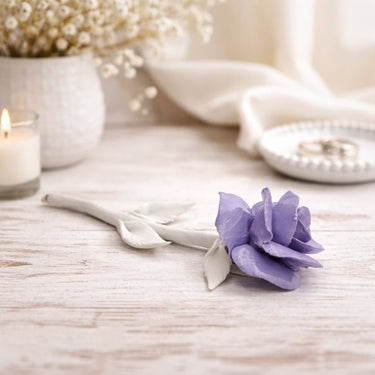 Purple Porcelain Rose on a white wood table with a candle and jewelry in the background