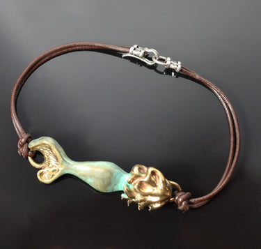 A handmade mermaid-themed bracelet featuring a brown leather cord, a gold-toned lion head charm, and a central turquoise and gold mermaid tail charm, displayed on a dark background.