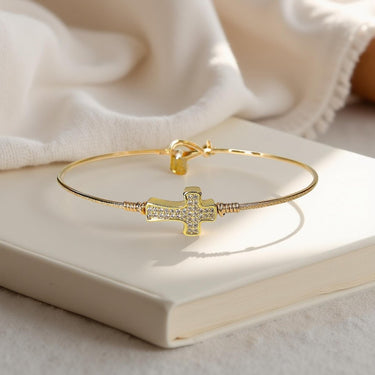 Gold bracelet with a cross charm on a white surface