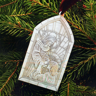 Decorative ornament with stained glass design of a woman holding a child, hanging on a Christmas tree.