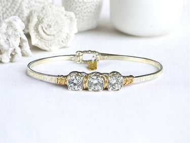 Gold bracelet with three clear gemstones on a white background