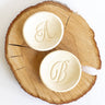 Two round soap bars with monogram designs on a wooden surface