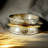 Set of three metallic rings with a textured finish on a textured fabric background