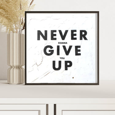 Framed artwork with 'NEVER GONNA GIVE YOU UP' text on a white wall.