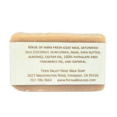 Bar of Natural goat milk soap with ground oatmeal exfoliation with a label detailing ingredients and contact information on a white background