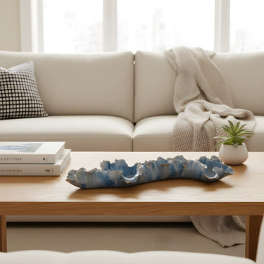 Beige sofa with a wooden coffee table featuring a Coral Beach Sculpture, books, and a plant.