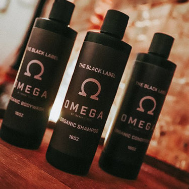 Three bottles of 'The Black Label Omega' organic hair care products on a wooden surface.