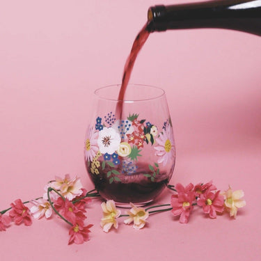 Painted Floral Stemless Wine Glass being filled with red wine on a pink background