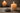 Two lit candles on a wooden surface with a stone in the foreground.