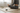 Person meditating on a yoga mat with a stone object in a room.