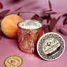 Peach Bellini Soy Candle in Blush Mercury Glass Jar with peach and branded coaster on a pink background