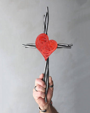 Hand holding a cross with a red heart design against a gray background