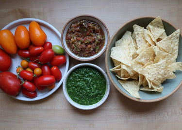 Assorted vegetables, salsa, and tortilla chips on a wooden surface
