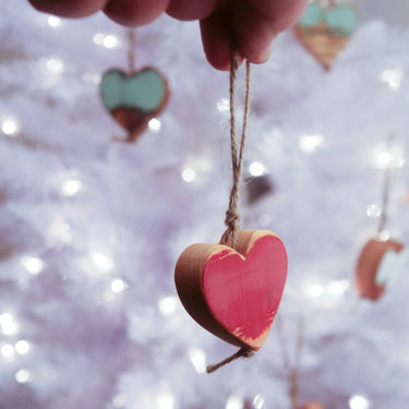 Hand holding a pink heart-shaped wooden ornament against a blurred light background